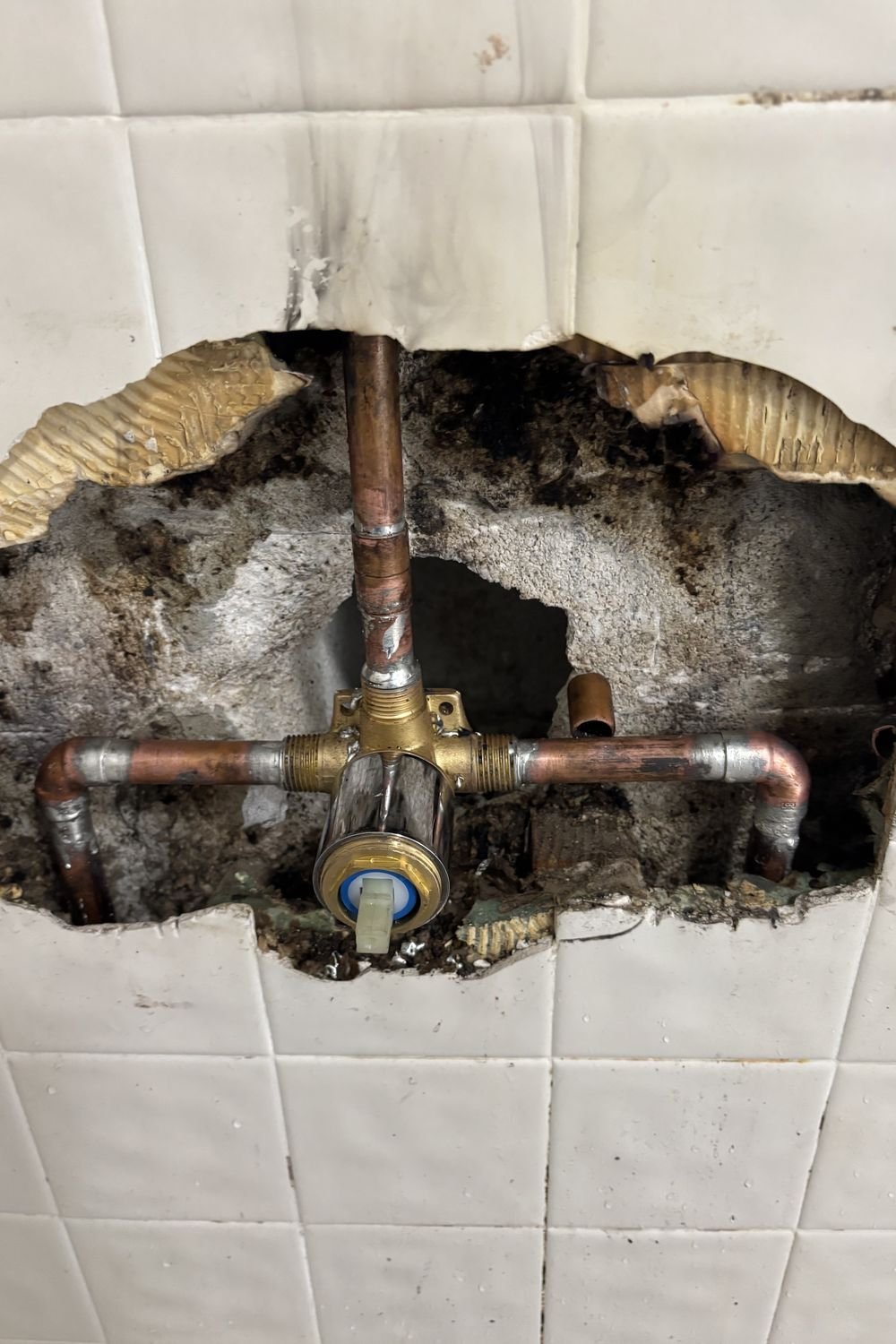 A shower wall opened through the tile, exposing copper supply lines and a newly fitted brass mixing valve.